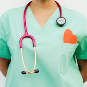 Close-up of a medical professional with a stethoscope and a paper heart cutout on a green uniform pocket.
